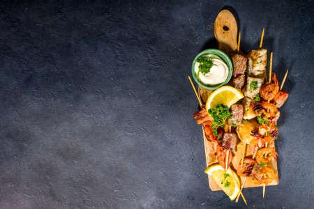 Assortment various barbecue Mediterranean grill food - fish, shrimp, crab, mussels, kebabs with sauces, black concrete background, above copy spaceの写真素材