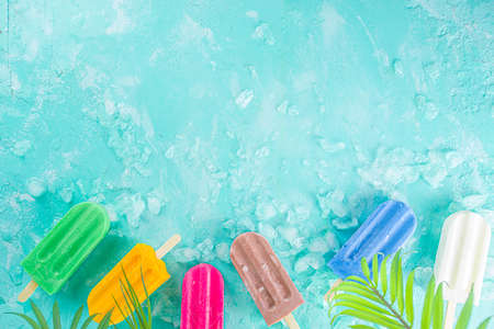 Selection of bright multicolored ice cream popsicle. Various gelato, frozen lollypops - chocolate vanilla blueberry strawberry pistachio orange, with crushed ice on light blue sunny backgroundの写真素材