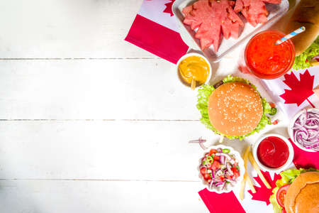 Set of various Canada Day bbq food. Picnic party table with maple leaf shaped watermelon, flags, burgers, hot dogs, fries and sauces, cold drinks, white table with red decor, top view copy spaceの写真素材