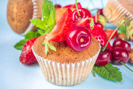 Summer baking concept, homemade vanilla white muffins with berry - strawberry, cherry, and mint, on baking sheet, light blue background top view copy spaceの写真素材