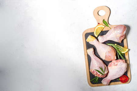 Raw uncooked chicken legs, drumsticks with spices and herbs for cooking, white table background top...
