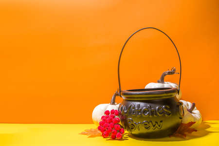 Halloween holiday simple background. Witch's cauldron bucket for collecting sweets candy, with autumn decor, pumpkins on a bright orange yellow background, cop space for textの写真素材
