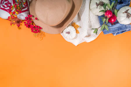 Autumn clothing cozy fashion concept. Warm white sweater, jeans, sneakers with autumn decor on a bright orange background top view flatlayの写真素材