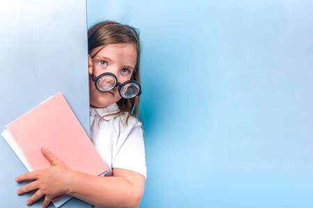 Back to school concept. School invitation, advertisement banner. Cute primary student schoolgirl in white blue classic uniform, funny glasses. Colorful bright blue trendy background copy spaceの写真素材