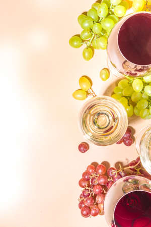 Glasses of red and white wine with sunshine and shadows, with bottle and decanter, bunch of grapes, on creamy color background, flatlay top view Wine tasting, autumn harvest, winery conceptの写真素材