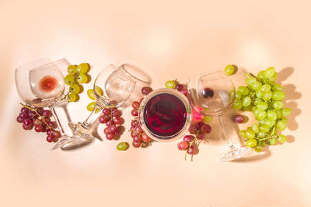 Glasses of red and white wine with sunshine and shadows, with bottle and decanter, bunch of grapes,...