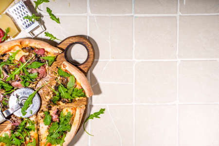 Homemade pizza with mushrooms, bacon, arugula and cheese, on tile summer sunny background. Girl's...