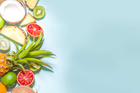 Summer vitamin food concept, various fruit and berries background - watermelon pineapple apples kiwi coconut orange lime creative flat lay on light blue background top view copy spaceの写真素材