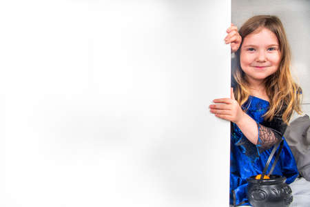 Autumn holiday Halloween invitation, greeting card background. Happy Caucasian child girl in a dress and a witch hat, with buckets of sweets copy spaceの写真素材