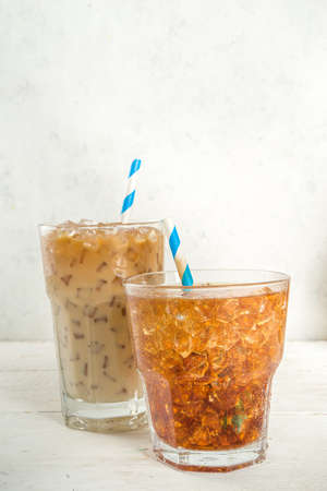 Set with different iced summer coffee drinks - espresso, frappe, latte, cappuccino, with whipped cream, syrup and crushed ice, in various glasses and mugs on white background copy space