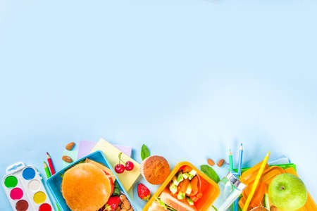 Back to school, Healthy tasty kid lunch box with sandwiches, nuts, fresh fruits and vegetable sticks. With school supplies, pencils, notebooks, on bright blue background flatlay top view copy spaceの写真素材