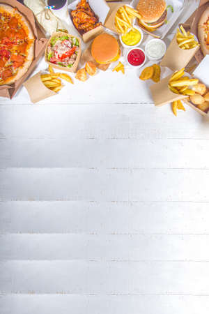 Delivery fastfood ordering food online concept. Large set of assorted take out foods pizza, french fries, fried chicken nuggets, burgers, salads, chicken wings, various sides, white table backgroundの写真素材