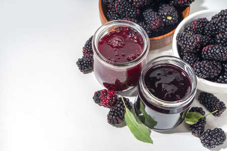Sweet homemade blackberry jam in small glass jar on a white background, with fresh berries copy spaceの写真素材