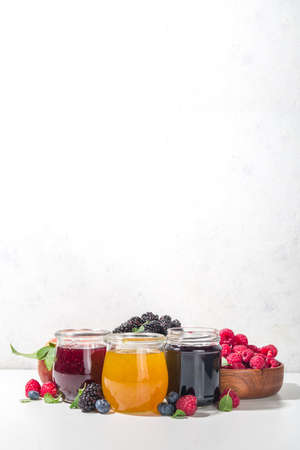 Assortment of summer seasonal berry and fruits jams in small jars, homemade preserving concept, marmalades or confitures with fresh berries on white background copy spaceの写真素材