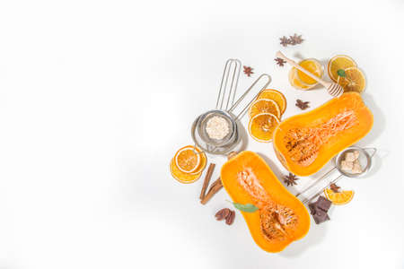 Autumn baking concept, raw ingredients for cooking sweet fall desserts, pies - pumpkin halves, spices, sugar, oats, eggs, flour, white background copy spaceの写真素材