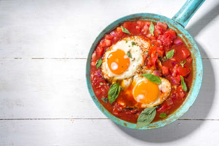 Traditional greek food, Shakshouka. eggs poached in frying pan with tomatoes, olive oil, peppers, onion, garlic, Mediterranean cuisine. Keto, fodmap low carb diet recipe, white wooden backgroundの写真素材