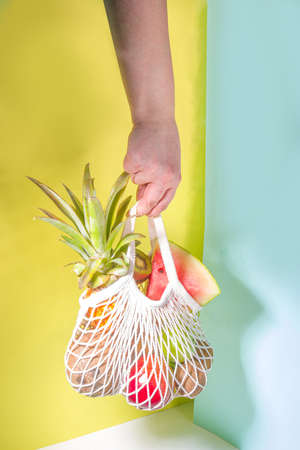 Summer fruit shopping background. Eco-friendly shopping bag full of fresh tropical fruits, on modern bright background with hard light copy space. Vitamin, healthy diet food conceptの写真素材