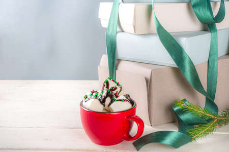 Big stack of Christmas gifts with hot chocolate, stay on it like pedestal, cozy pastel colored craft paper gift boxes with green festive Xmas ribbon, cup of cocoa with marshmallow, copy spaceの写真素材