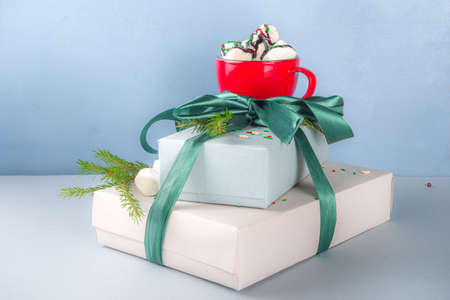 Big stack of Christmas gifts with hot chocolate, stay on it like pedestal, cozy pastel colored craft paper gift boxes with green festive Xmas ribbon, cup of cocoa with marshmallow, copy spaceの写真素材