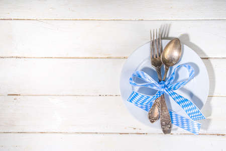 October fest concept. Oktoberfest table setting background, plate fork knife spoon with traditional napkin, beer mug. served at event,  bar menu flatlay, white wooden table copy space top viewの写真素材