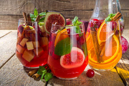 Traditional autumn winter drink hot spicy sangria - red, pink, white. With cider, pink red wine, apples, oranges, pomegranate, cranberry, plum, figs, cinnamon sticks. Wooden rustic table copy spaceの写真素材
