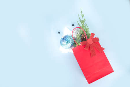 Simple Xmas greeting card, party invitation, sale abstract flatlay with disco Christmas balls, fir tree branches, paper bag with festive bow, on light blue background copy space top viewの写真素材