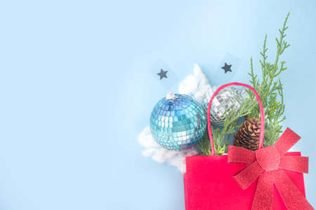 Simple Xmas greeting card, party invitation, sale abstract flatlay with disco Christmas balls, fir tree branches, paper bag with festive bow, on light blue background copy space top view
