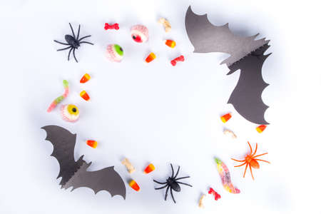 Happy Halloween day holiday background. Flat lay with sweets and decorations for kids party, bucket pack with spiders, candy sweets, bat, on white table copy space top view frameの写真素材