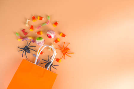 Happy Halloween day holiday background. Flat lay with sweets and decorations for kids party, bucket pack with spiders, candy sweets, bat, on colorful orange paper copy space top viewの写真素材