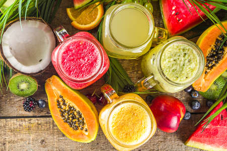 Assorted different fruit smoothies and juices with tropical fresh fruits and berries. Clean eating, healthy lifestyle, diet and vitamin drink beverages concept. Top view flatlay white table backgroundの写真素材