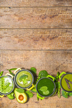 Green cream-soup set. Variety of classic green vegetable soups, in small portioned pots - asparagus, spinach, broccoli, green peas. over wooden background copy space top viewの写真素材