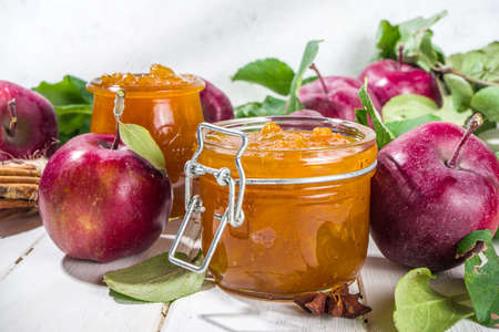 Homemade golden colored apple jam, with farm red apples and leaves on white wooden background copy spaceの写真素材