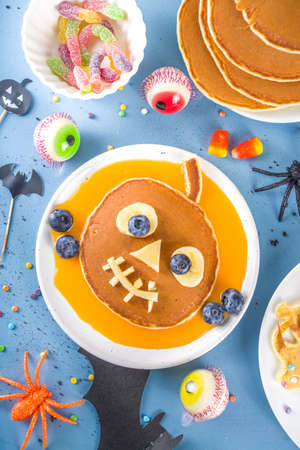 Creative homemade Halloween pancakes for breakfast, in form of funny monsters, ghost, bat, witch. With traditional trick or treat sweets, candy and decorations, top view on colorful blue backgroundの写真素材
