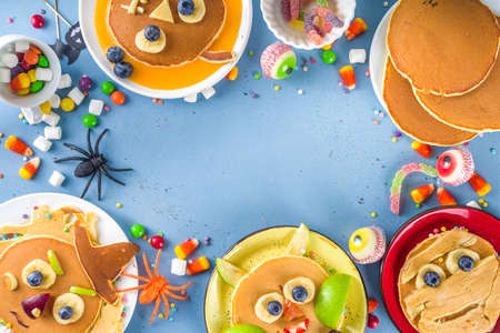 Creative homemade Halloween pancakes for breakfast, in form of funny monsters, ghost, bat, witch. With traditional trick or treat sweets, candy and decorations, top view on colorful blue backgroundの写真素材