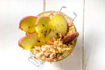 Autumn apple pecan oatmeal, overnight oats porridge with red apples, pecan nuts and caramel sauce, white wooden background copy spaceの写真素材
