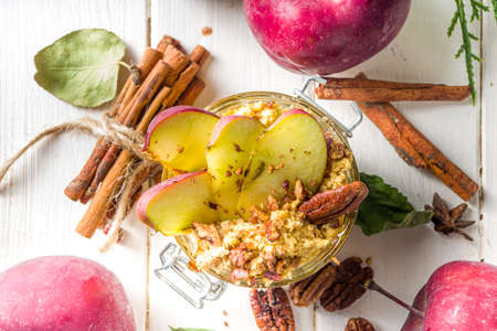 Autumn apple pecan oatmeal, overnight oats porridge with red apples, pecan nuts and caramel sauce, white wooden background copy spaceの写真素材
