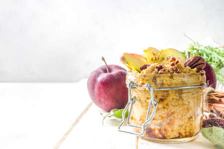 Autumn apple pecan oatmeal, overnight oats porridge with red apples, pecan nuts and caramel sauce, white wooden background copy spaceの写真素材