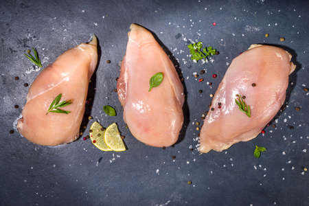 Raw chicken breast filet on dark concrete background with spices and herbs for cooking, top view copy spaceの写真素材