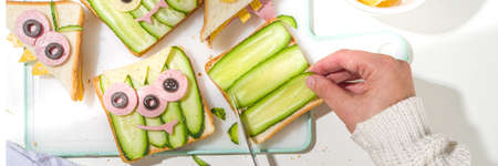 Various funny monster Halloween sandwiches. Cooking creative breakfast snack toasts with cheese, Halloween kids party food, mother woman hands in picture top viewの写真素材