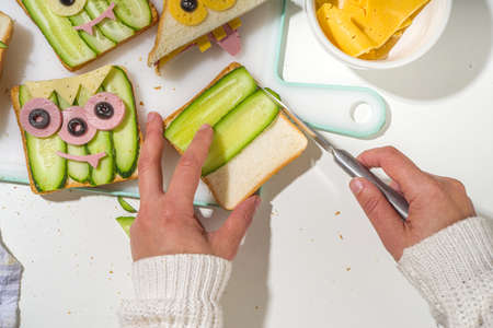Various funny monster Halloween sandwiches. Cooking creative breakfast snack toasts with cheese, Halloween kids party food, mother woman hands in picture top viewの写真素材
