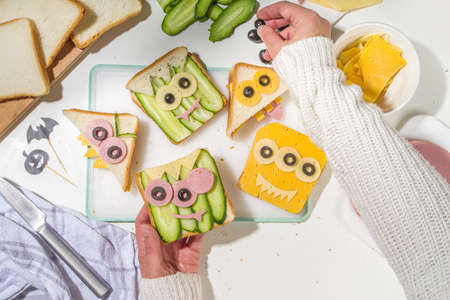 Various funny monster Halloween sandwiches. Cooking creative breakfast snack toasts with cheese, Halloween kids party food, mother woman hands in picture top viewの写真素材