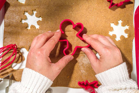 Christmas, New Year cooking background. Baking ingredients and utensils - gingerbread dough, cookie cutters, rolling pin. Woman hands making festive Xmas sweet cookies bright festive red white conceptの写真素材
