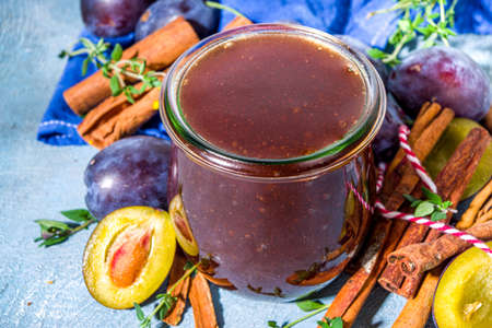 Spicy autumn plum jam in small jar, with cinnamon, thyme, anise and fresh plums on concrete blue background copy spaceの写真素材