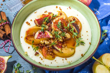 Autumn breakfast or snack, spicy semolina porridge with caramelized apples, grilled peach, plums and figs, nut, thyme, honey. Top view on blue sun lighted concrete tableの写真素材