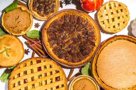 Set variety autumn pies. Pecan, apple, pumpkin small tart cakes and pies on concrete background with bright sun light, dark shadows top viewの写真素材