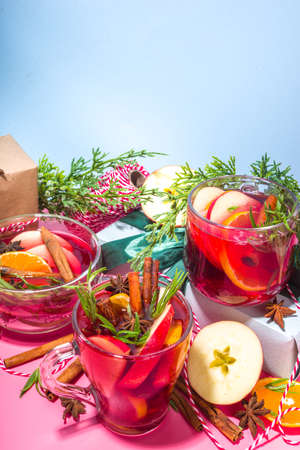 Homemade mulled wine cocktail. Various glass mugs with classic winter hot spicy mulled wine, with ingredients, Christmas decor and gift boxes on high-colored modern backgroundの写真素材