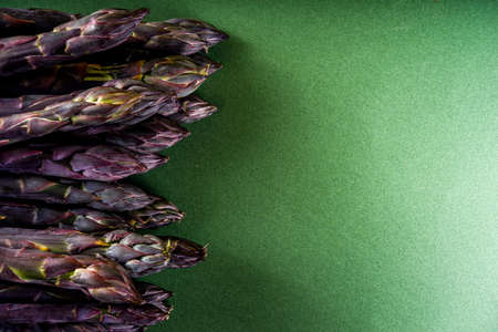 Fresh raw organic asparagus bunch, purple, green and white vegetable on dark green background