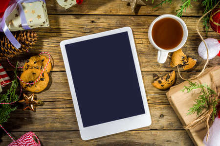 Santa hands with tablet pc, christmas decoration and lot of gift boxes, wishlist and preparation for...