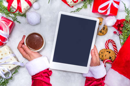 Creative layout frame with lot gift boxes, christmas tree branches, pine cones, hot chocolate mug, xmas sweet, tablet pc on white fluffy fur background. Xmas and New Year preparation backgroundの写真素材