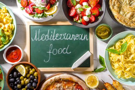Set of different Mediterranean foods: olives, mozzarella tomato salad, Greek salad, pasta, tortellini ravioli, pizza, pita sandwich, shish kebab, shakshuka, hummus, top viewの写真素材